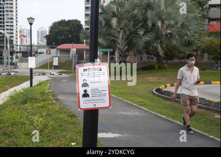 29.04.2020, Singapur, Republik Singapur, Asien, Ein Mann mit Gesichtsmaske geht an einem COVID-19-Schild vorbei, das obligatorische Maßnahmen zur weiteren Limi anzeigt Stockfoto