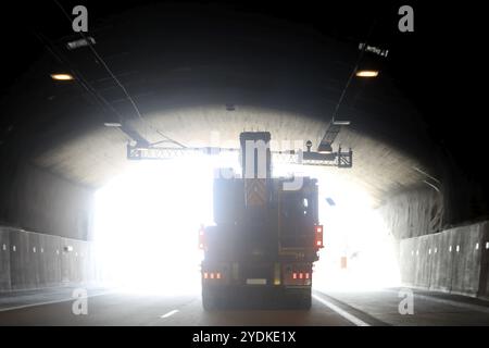 Sattelauflieger, der eine übergroße Ladung gegen Tageslicht am Ende eines Autobahntunnels transportiert Stockfoto