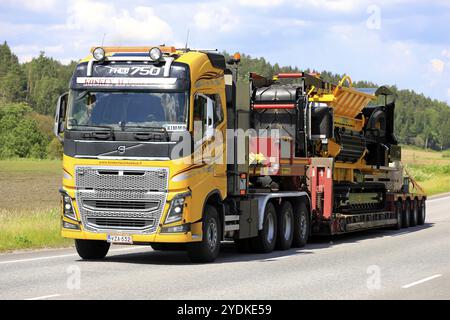 Der gelbe Volvo FH16 Truck Kosken Autokeskus transportiert den Tana Shark Abfallhäcksler auf einem Tieflader als breite Ladung. Road 52, Salo, Finnland. Juni 2021 Stockfoto