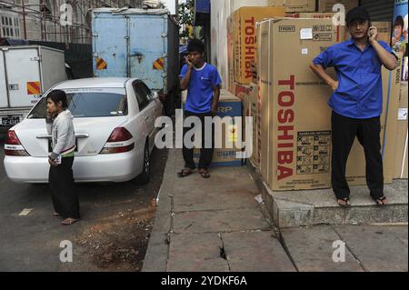 28.01.2014, Yangon, Myanmar, Asien, drei Personen sprechen gleichzeitig am Telefon auf dem Bürgersteig vor einem Haushaltswarenladen. Importiertes Produkt Stockfoto