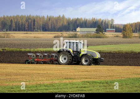 Bauer pflügt Feld mit grünen Valtra Traktor und Pflügen an einem sonnigen Herbstmorgen in Südfinnland. Jokioinen, Finnland. Oktober 2020 Stockfoto