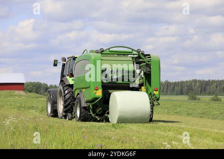 Salo, Finnland. Juni 2019. Deutz-Fahr Traktor und McHale 3 plus Ballenpressensilage in grüner Kunststoffplatte auf dem Heufeld an einem sonnigen Sommertag Stockfoto