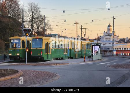 Zwei HSL-Straßenbahnen, 2 und 3 am Olympia-Terminal, halten an einem ruhigen Morgen bei Sonnenaufgang, im Hintergrund der Kathedrale von Helsinki. Helsinki, Finnland. April 2020 Stockfoto