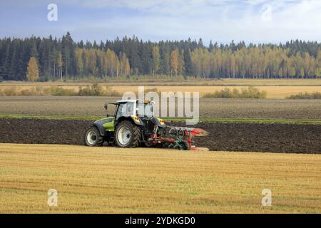 Bauer pflügt Feld mit grünen Valtra Traktor und Pflügen an einem sonnigen Herbstmorgen in Südfinnland. Jokioinen, Finnland. Oktober 2020 Stockfoto