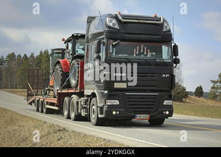 SALO, FINNLAND, 14. APRIL 2017: Schwarzer DAF XF 105 Sattelzug transportiert landwirtschaftliche Traktoren und kleine Bagger auf Schwanenhals-Anhänger entlang ländlicher Highwa Stockfoto