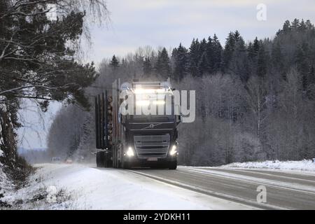 Der neue, schwarze Volvo FH16 Holzfäller von Transport A Bjoerkqvist transportiert Holzlast auf der Straße, Fernlicht ist kurz eingeschaltet. Salo, Finnland. Dezember 2021 Stockfoto