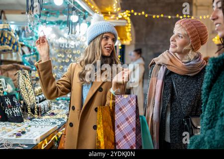 Vielfältige Freunde genießen Weihnachtseinkäufe auf einem lebhaften Nachtmarkt voller festlicher Lichter. Sie lächeln und teilen fröhliche Momente und erkunden den Urlaub Stockfoto