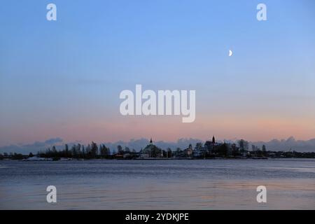 Mond im ersten Viertel über der Ostsee nach Sonnenuntergang an einem blauen Winternachmittag. Vom Südhafen aus gesehen, Helsinki, Finnland, am Horizont, Valkosaari isl Stockfoto