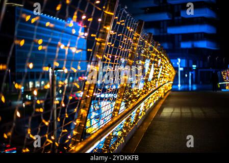 Nahaufnahme von kleinen farbigen Lichtern auf Metallgitter mit gelben blauen und roten Farben auf der Balustrade einer Stadtbrücke im Hintergrund Stadtgebäude mit Stockfoto