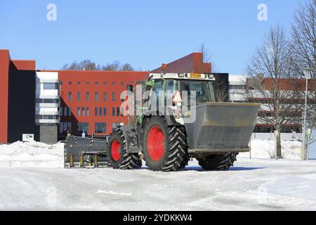 Traktor verteilt Körnung mit ATI 18 Streuer und pflügt Schnee vom Parkplatz nach Schneefall. Rückansicht. Salo, Finnland. März 2023 Stockfoto