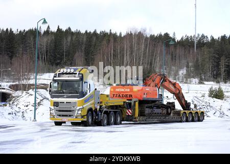 Salo, Finnland, 9. März 2019: Gelber Volvo FH16 Mantyla auf einem Hof, der bereit ist, an einem Wintertag eine große Ladung Hitachi ZX 350LC Raupenbagger zu transportieren. Stockfoto