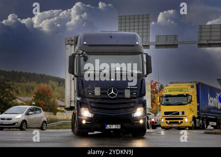 Straßenkreuzung mit schwarzem Mercedes-Benz Actros-Gütertransporter. Regnerisches Wetter, helle Scheinwerfer, dunkle Wolken. Salo, Finnland. Septe Stockfoto