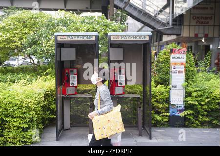 12.03.2020, Singapur, Republik Singapur, Asien, Eine Frau läuft an zwei öffentlichen Telefonzellen auf der Orchard Road vorbei und trägt eine Maske, um sich zu schützen Stockfoto