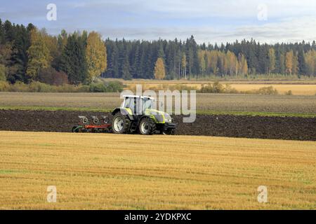 Bauer pflügt Feld mit grünen Valtra Traktor und Pflügen an einem sonnigen Herbstmorgen in Südfinnland. Jokioinen, Finnland. Oktober 2020 Stockfoto