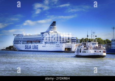 Die Silja Symphony Kreuzfahrtfähre legt im Südhafen an und die Suokki Helsinki-Suomenlinna Fähre segelt an einem sonnigen Tag. Helsinki, Finnland. Juni 2017 Stockfoto