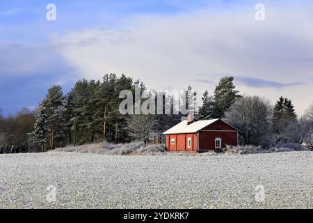 Kleines rotes Landhaus an einem leicht schneebedeckten Feld an einem schönen Tag des frühen Winters, mit einigen Wolken am Himmel. Salo, Finnland. November 30, 2019 Stockfoto