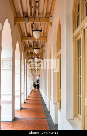 Leute gehen an der Straße entlang, die Bögen entlang der Fassade des Raffles Hotels in Singapur sehen Stockfoto