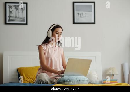 Asiatische Frau, die sich auf dem Bett mit Laptop zu Hause entspannt Stockfoto