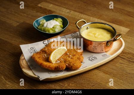 Eine köstliche Portion goldbrauner Schnitzel mit Zitronenkeil, dazu cremiges Kartoffelpüree in einem Kupfertopf und eine Seite Gurkensalat mit Stockfoto