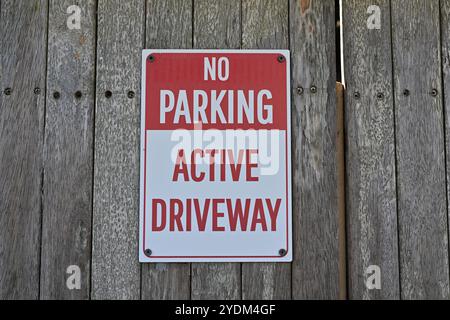 Rot-weißes rechteckiges, rechteckiges Schild, kein Parken, aktive Auffahrt an einem Holztor, im Schatten Stockfoto