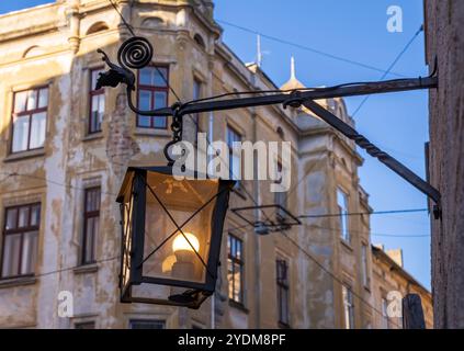 Dämmerungswächter: Antike Lampe im historischen Viertel. Viktorianische Lampe gegen veraltete Fassade. Vintage-Laterne aus Eisen, die an der Betonwand hängt Stockfoto