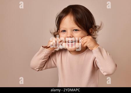 Lächelndes Mädchen isst Fruchtpastille auf beigem Hintergrund. Gesunde Babynahrung. Stockfoto