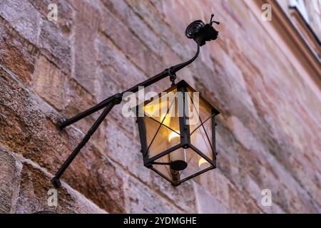 Twilight's Keeper: Vintage Street Illumination. Viktorianische Lampe gegen veraltete Fassade. Vintage-Laterne aus Eisen, die an einer Betonwand hängt Stockfoto