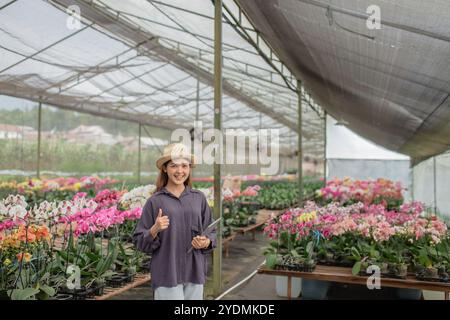 Fröhliche junge Frau im Blumengewächshaus, umgeben von bunten Orchideen Stockfoto