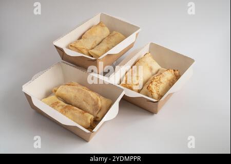 Drei Take-Out-Kisten gefüllt mit ordentlich gefalteten Crepes, bereit für Lieferung oder zum Mitnehmen, fotografiert vor einem schlichten Hintergrund. Stockfoto