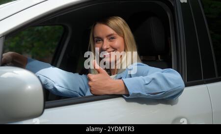 Glückliche positive kaukasische Fahrerin lächelnde Käuferin, die Auto-Testfahrt fährt Mädchen Geschäftsfrau Lenkerin, die Daumen nach oben zeigt Stockfoto