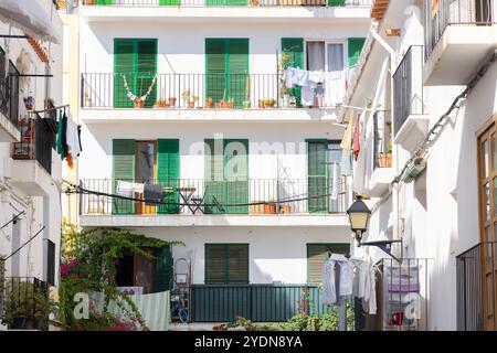 Charmante Wohnszene in Ibiza-Stadt, mit traditionellen Balkonen mit grünen Fensterläden und farbenfroher Kleidung, die in der mediterranen Sonne trocknet. Stockfoto