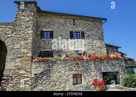 Eine Fülle von Blumen fließt von einem Balkon eines Steingebäudes im mittelalterlichen Weiler aus dem 14. Jahrhundert am französischen Ufer des Genfer Sees im kleinen Dorf Yvoire, Haute Savoie, Frankreich. Stockfoto