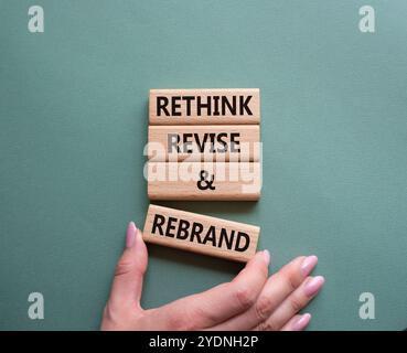 Überdenken Sie das Symbol „Überarbeiten“ und „Rebranding“. Holzblöcke mit Wörtern überdenken und neu gestalten. Geschäftsmann Hand. Wunderschöner graugrüner Hintergrund. Unternehmen und Stockfoto