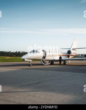 Vorderansicht des Business Jet auf dem Vorfeld des Flughafens am Morgen. Die dunkle Morgensonne wirft lange Schatten auf die Betonoberfläche. Stockfoto