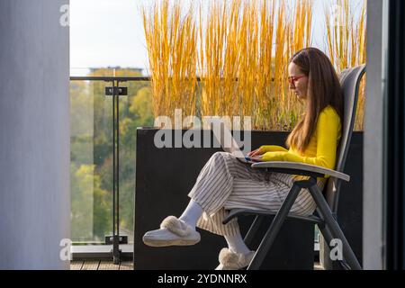 Eine junge kaukasische Frau arbeitet auf ihrem Laptop, während sie auf einem Balkon in Prag sitzt. Authentisches Zuhause. Stockfoto