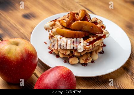 Belgische Waffeln mit Äpfeln in Wein gedünstet mit Weinsauce auf einem weißen Teller auf hölzernem Hintergrund. Hochwertige Fotos Stockfoto