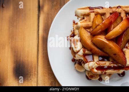 Belgische Waffeln mit Äpfeln in Weinsauce gedünstet auf einem weißen Teller auf hölzernem Hintergrund. Platz für Text. Hochwertige Fotos Stockfoto