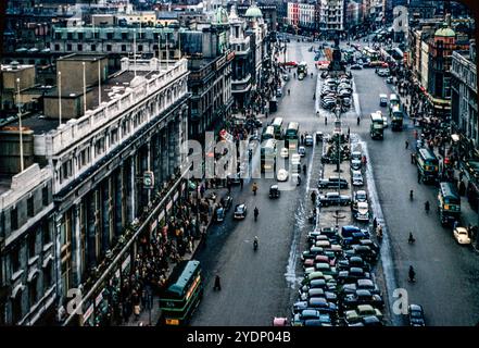 Ein Foto von einer geschäftigen O’Connell Street in Dublin, Irland, das 1957 von Nelson’s Pillar aufgenommen wurde und auf der linken Seite Clery’s Department Store zeigt. Autos stehen in der Mitte der Straße und auf der linken Straßenseite. Die grünen Busse wurden dann von Córas Iompair Eireann betrieben. Weiter unten befindet sich die Kreuzung der O’Connell Street und der Quays, wo der Verkehr auf beiden Seiten des Batchelor's Walk verkehrt. Stockfoto