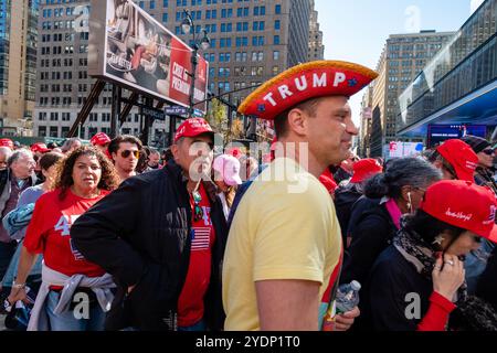 New York, NY, USA. Oktober 2024. Vor dem Madison Square Garden versammeln sich vor einer abendlichen Kundgebung Massen von Anhängern Donald Trump, von denen viele Mützen und Hemden der Marke MAGA oder Trump tragen. Eine Gruppe von Teilnehmern überquert die 8. Avnue. Quelle: Ed Lefkowicz/Alamy Live News Stockfoto