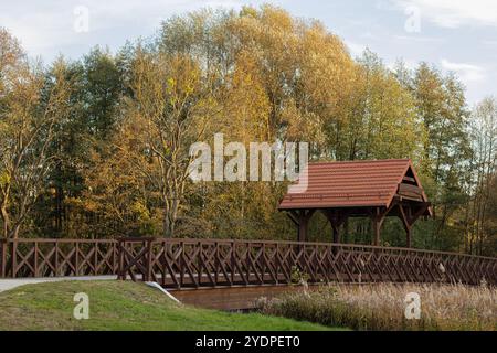 Malerische Holzbrücke mit rot gekacheltem Dach, umgeben von goldenen Herbstbäumen an einem sonnigen Tag in einem friedlichen Park Stockfoto