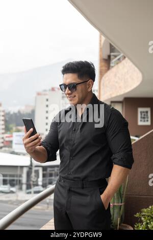 An einem sonnigen Tag mit Handy ein attraktiver junger Mann, trägt schwarzen Anzug und Sonnenbrille, Stadtleben, Geschäftsmann arbeitet Stockfoto