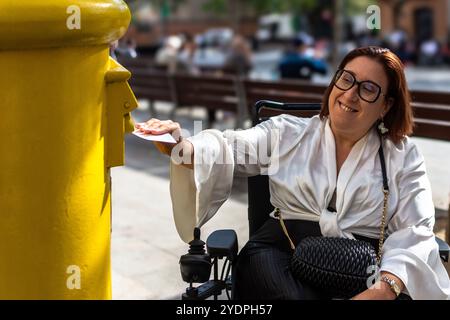 Frau im Rollstuhl lächelt, während sie einen Brief postet Stockfoto