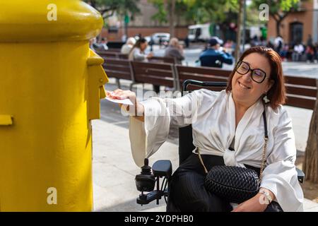 Weibliche Rollstuhlbenutzerin, die einen Brief in der städtischen Mailbox postet Stockfoto