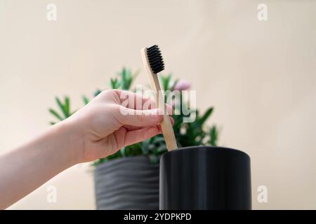 In seiner Hand steht eine hölzerne Zahnbürste in einem Glas Stockfoto