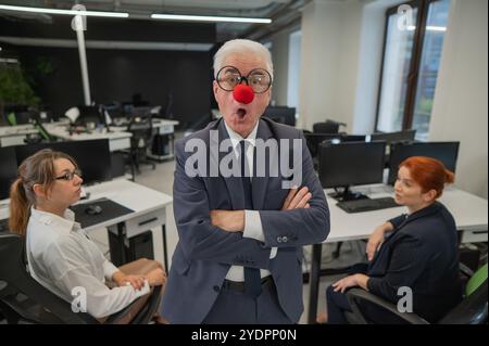 Ein älterer Mann in einem Clown-Kostüm macht sich auf der Arbeit lustig. Stockfoto