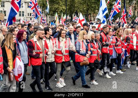 Englische Demonstranten mit verknüpften Waffen marschieren zum britischen parlament, um eine von Tommy Robinson unterstützte Pro-UK-Kundgebung durchzuführen. Oktober 2024, London, Großbritannien. Stockfoto