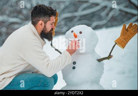 Schneemann und Winterspaß für den Menschen. Wintermann. Glücklicher Vater, der mit einem Schneemann auf einem verschneiten Winterspaziergang spielt. Junge Hipster-Winterporträt. Stockfoto