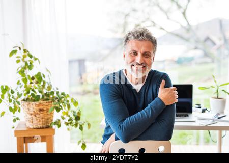 Homeoffice für einen schönen Mann. Mann sitzt rückwärts auf dem Stuhl und blickt in die Kamera. Telearbeit. Stockfoto