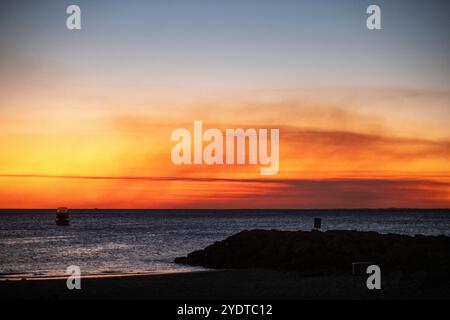 Dieses Bild fängt einen ruhigen Sonnenuntergang am Strand mit satten, warmen Farben und dem ruhigen Meer ein. Stockfoto
