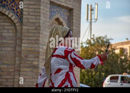 Buchara, Usbekistan; 19. September 2024: Eine usbekische Frau, die ein leuchtendes rotes Kleid und ein traditionelles Kopftuch trägt, während sie Fotos in der Geschichte macht Stockfoto